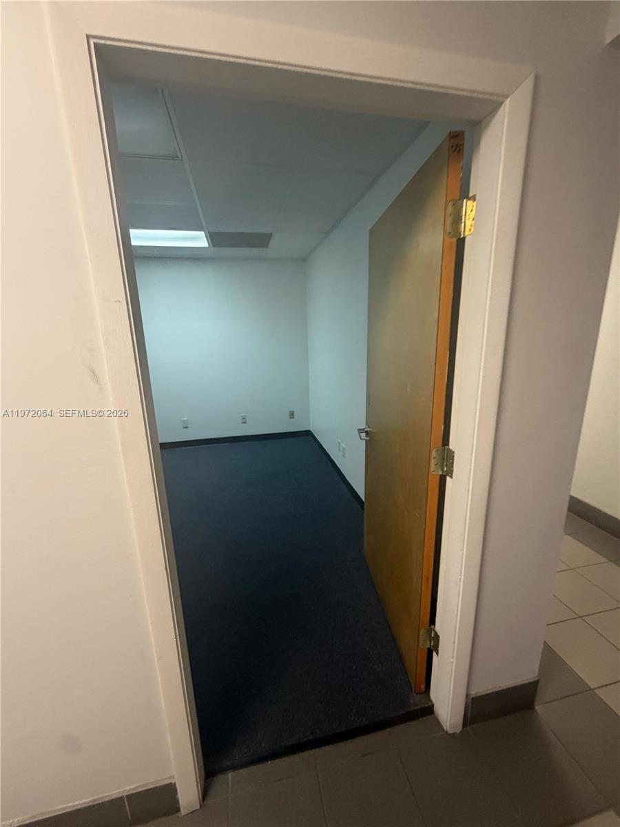 A small, empty office features dark blue carpeting, white walls, and a wooden door — 13449 NW 42nd Ave, Opa-Locka FL 33054, OPA-LOCKA, FL