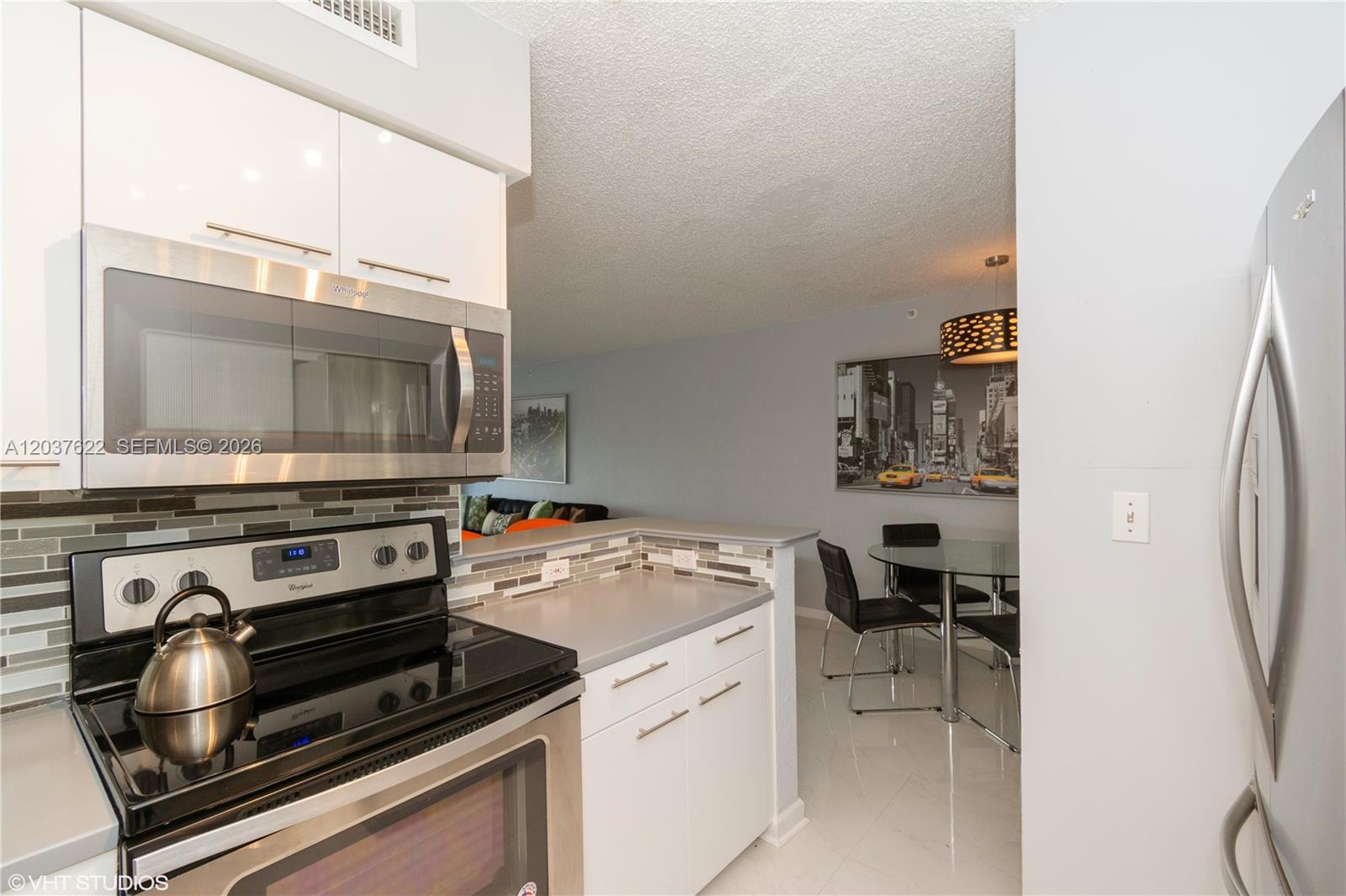 A kitchen with white cabinets and stainless steel appliances overlooks a dining area — 1500 Bay Rd # 654S, Miami Beach FL 33139, MIAMI BEACH, FL