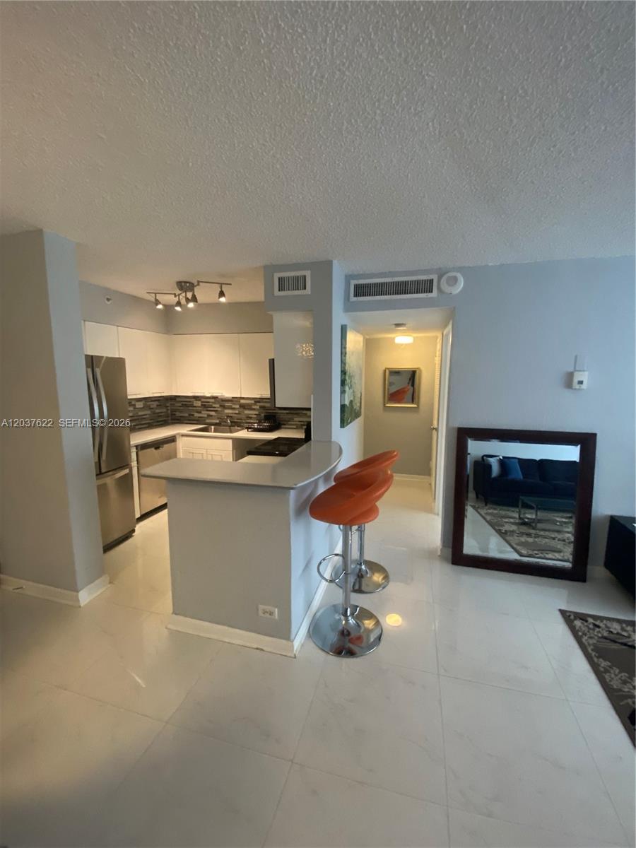 A kitchen with white cabinets and stainless steel appliances features a breakfast bar with stools — 1500 Bay Rd # 654S, Miami Beach FL 33139, MIAMI BEACH, FL