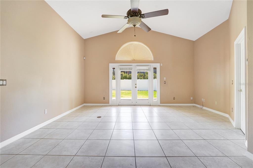 A living room with vaulted ceilings, tile flooring, a ceiling fan, and glass patio doors — 9720 NONACREST DRIVE, ORLANDO, FL