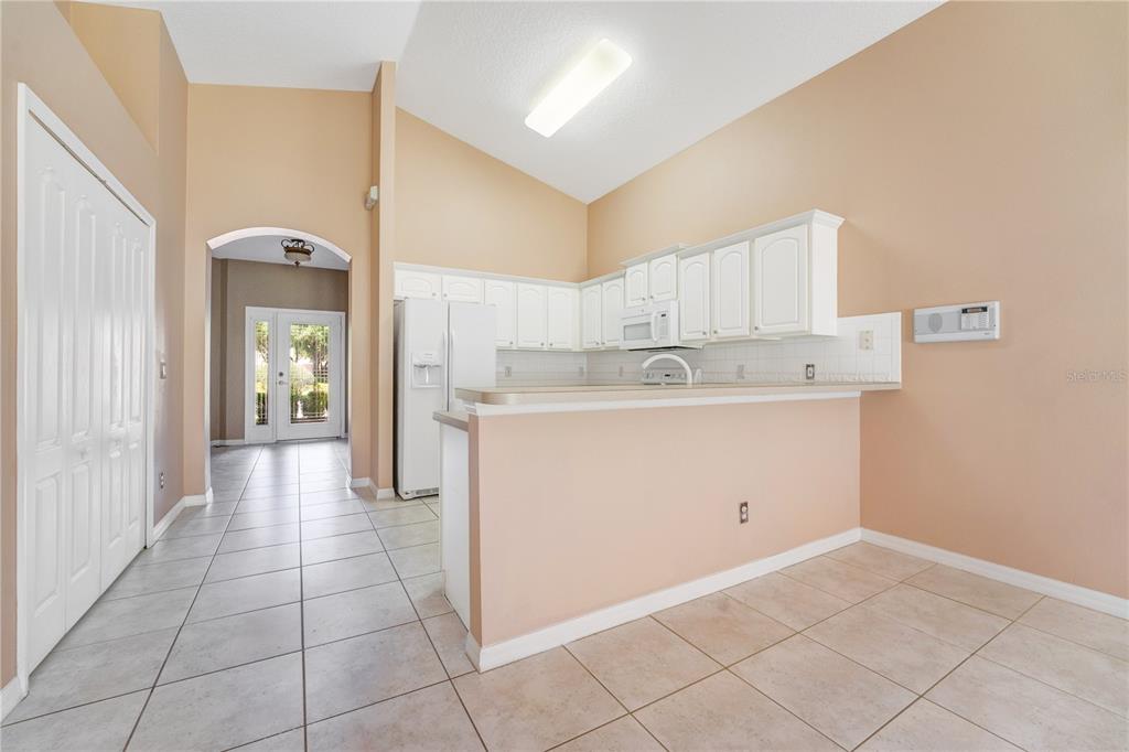 A kitchen with white cabinets, a breakfast bar, and tile flooring under a vaulted ceiling — 9720 NONACREST DRIVE, ORLANDO, FL