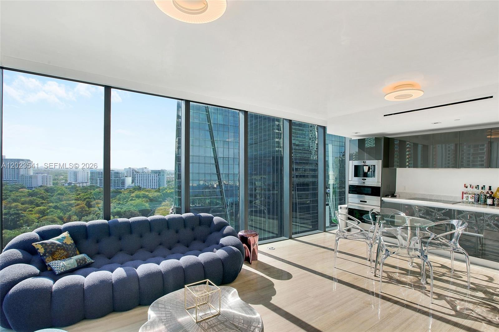 A modern living room and kitchen area features a blue sofa, glass table, and floor-to-ceiling windows — 1451 Brickell Ave # 1604, Miami FL 33131, MIAMI, FL