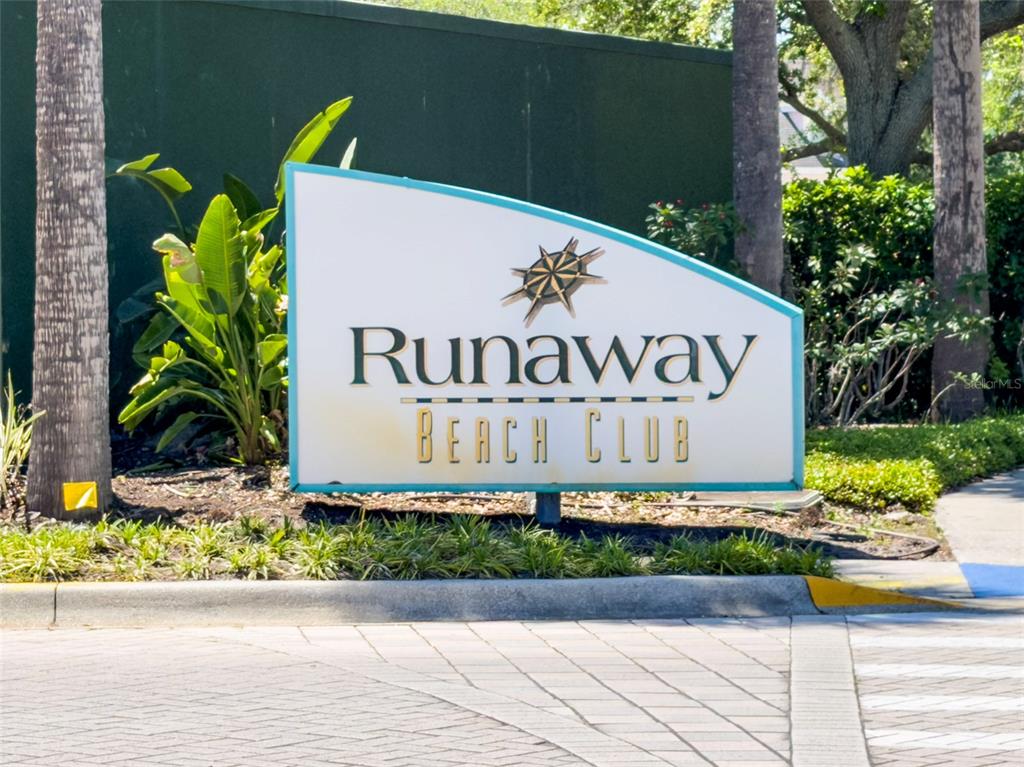A sign for Runaway Beach Club stands in a landscaped area with palm trees — 3002 LIMBO LANE UNIT 101, KISSIMMEE, FL