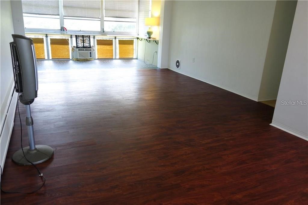 A spacious room features dark wood-look flooring, white walls, and a large windowed sunroom area — 200 N BETTY LANE UNIT 2E, CLEARWATER, FL