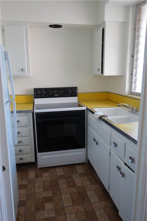 A kitchen features white cabinets, yellow countertops, a black electric stove, and a double sink — 200 N BETTY LANE UNIT 2E, CLEARWATER, FL