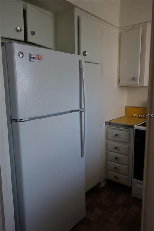 A white refrigerator stands next to white cabinets and a yellow countertop in a kitchen — 200 N BETTY LANE UNIT 2E, CLEARWATER, FL