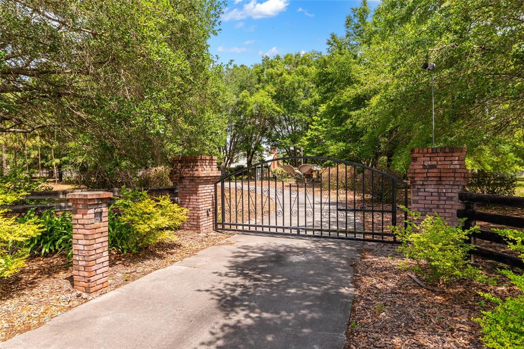 A paved driveway leads to a black metal gate flanked by brick pillars and trees — 272 NE COUNTY ROAD 337, TRENTON, FL