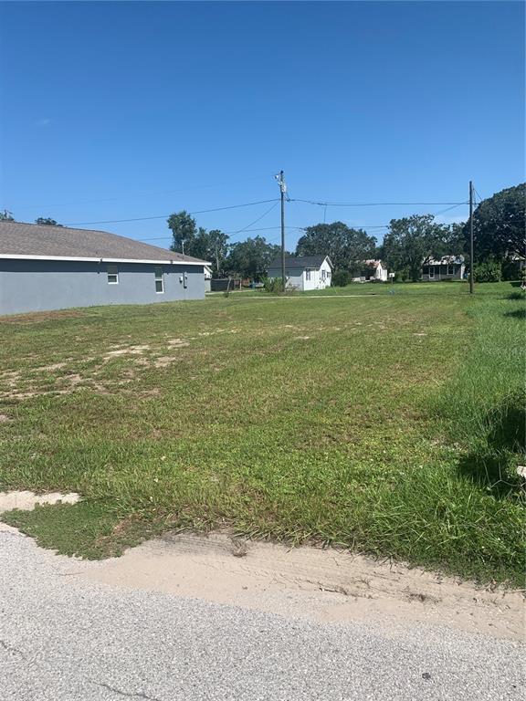 A vacant grassy lot sits next to a gray house under a clear blue sky — 517 LINCOLN AVENUE W, LAKE WALES, FL