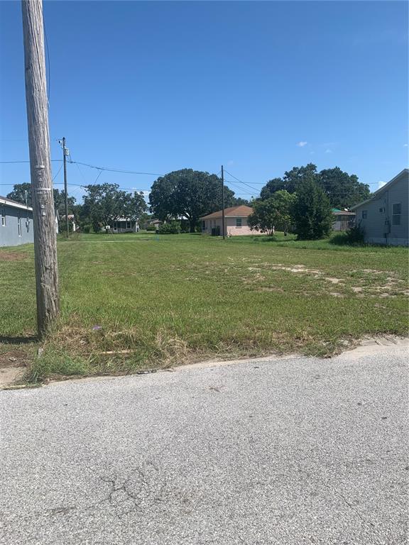 A vacant, grassy residential lot sits between two houses under a clear blue sky — 517 LINCOLN AVENUE W, LAKE WALES, FL