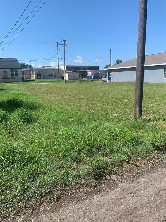 A vacant, grassy lot sits between two residential buildings under a clear blue sky — 517 LINCOLN AVENUE W, LAKE WALES, FL