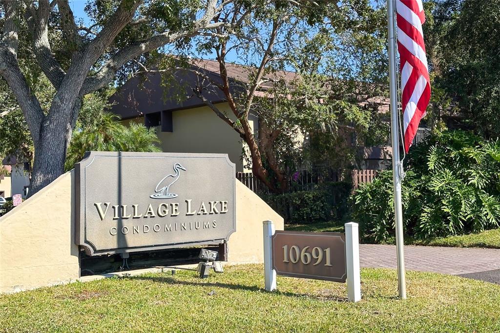 A sign for Village Lake Condominiums stands in front of a building and trees — 735 S VILLAGE DRIVE N UNIT 206, ST PETERSBURG, FL