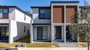 A modern two-story townhouse with white stucco walls, wood-look siding, and a dark front door — 3243 SUSTAINABLE WAY, KISSIMMEE, FL
