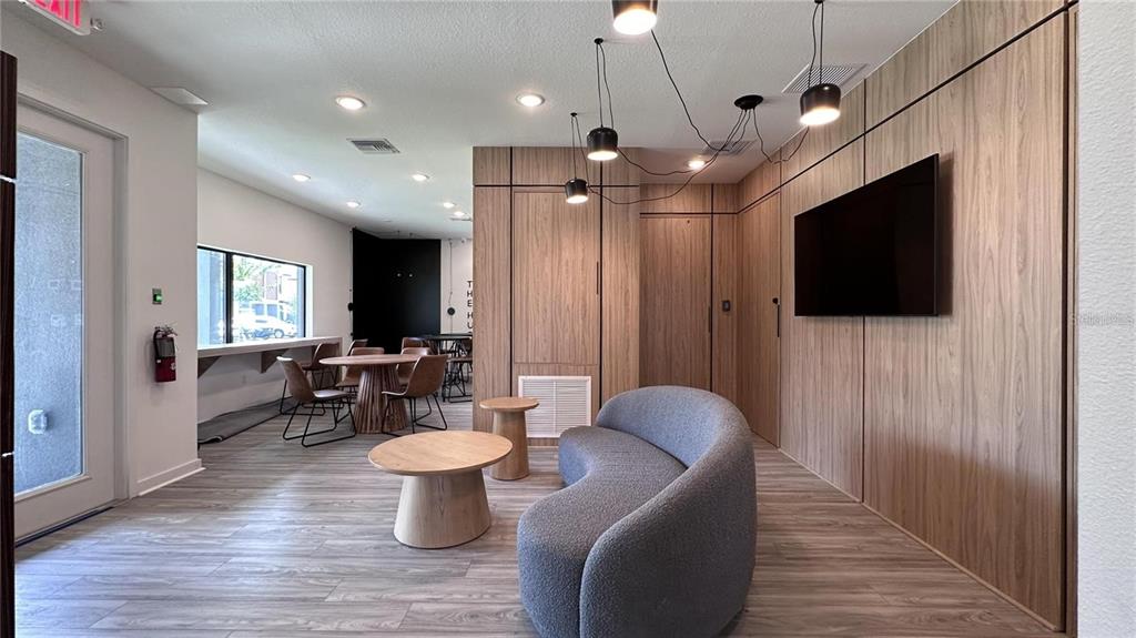 A modern lounge area features wood-paneled walls, a curved gray sofa, and pendant lighting — 3243 SUSTAINABLE WAY, KISSIMMEE, FL