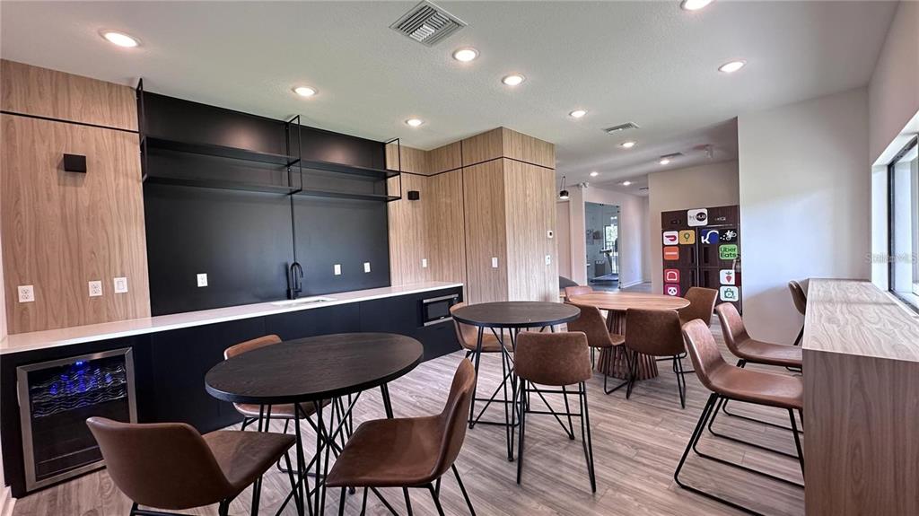 A modern communal lounge features dark cabinetry, round tables with brown chairs, and wood-paneled walls — 3243 SUSTAINABLE WAY, KISSIMMEE, FL