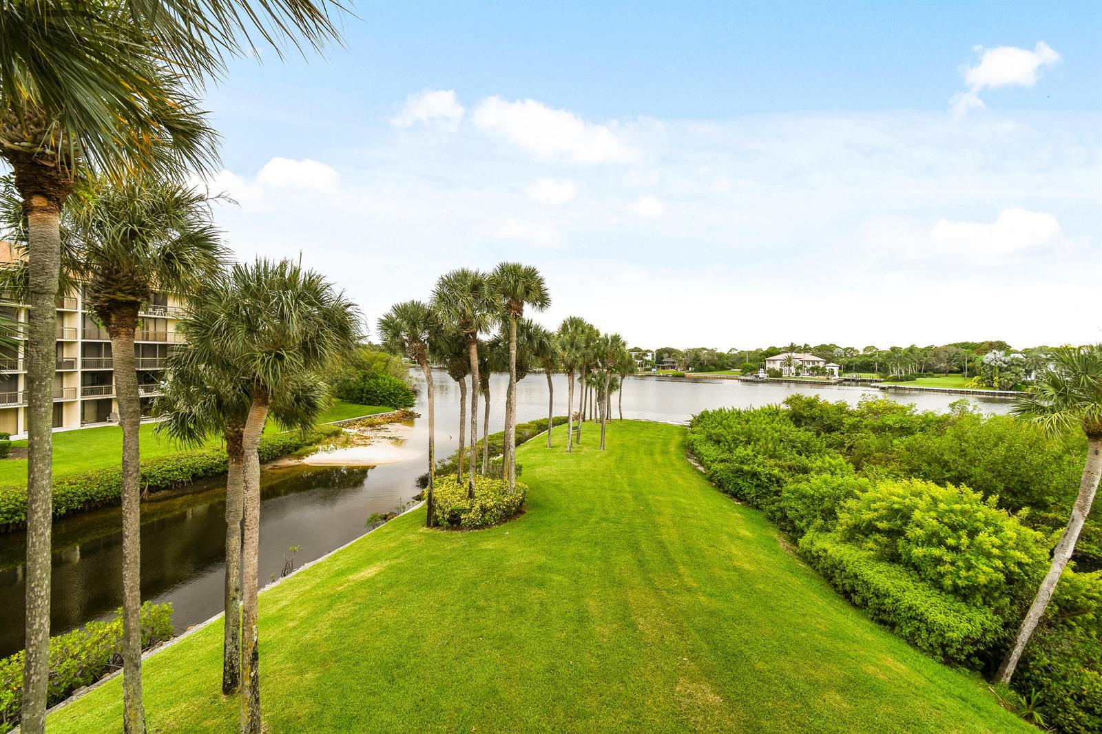 An elevated view of a grassy lawn, palm trees, and a canal leading to water — 1701 Marina Isle Way # 301, Jupiter FL 33477, JUPITER, FL