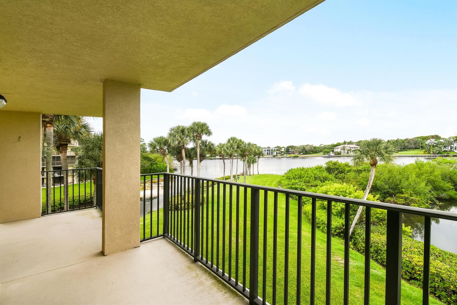 A covered balcony with a black metal railing overlooks a grassy lawn and a lake — 1701 Marina Isle Way # 301, Jupiter FL 33477, JUPITER, FL