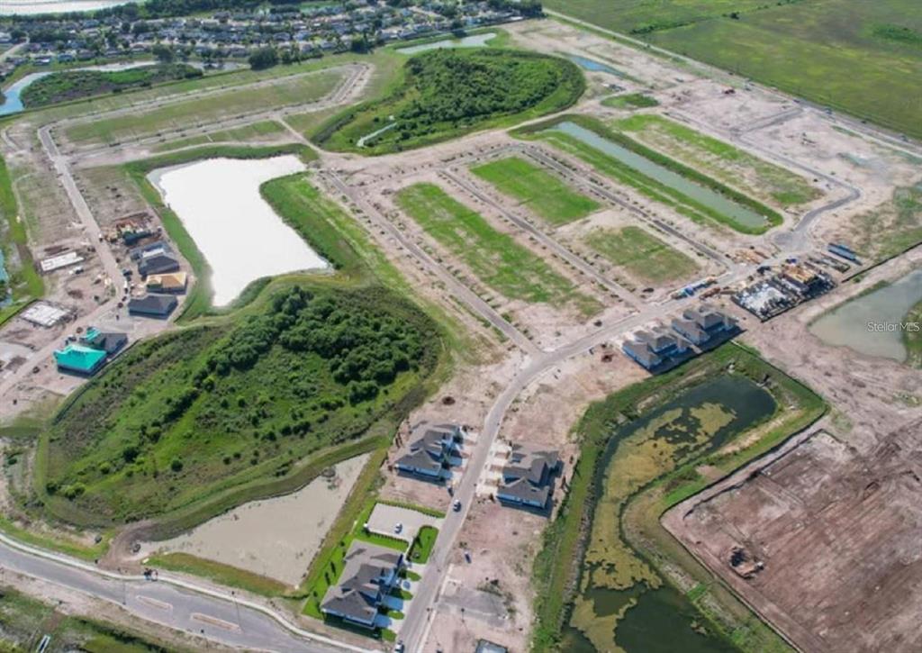 An aerial view shows a residential construction site with several houses, ponds, and cleared lots — 8132 SUNNY POINT TRAIL, PARRISH, FL