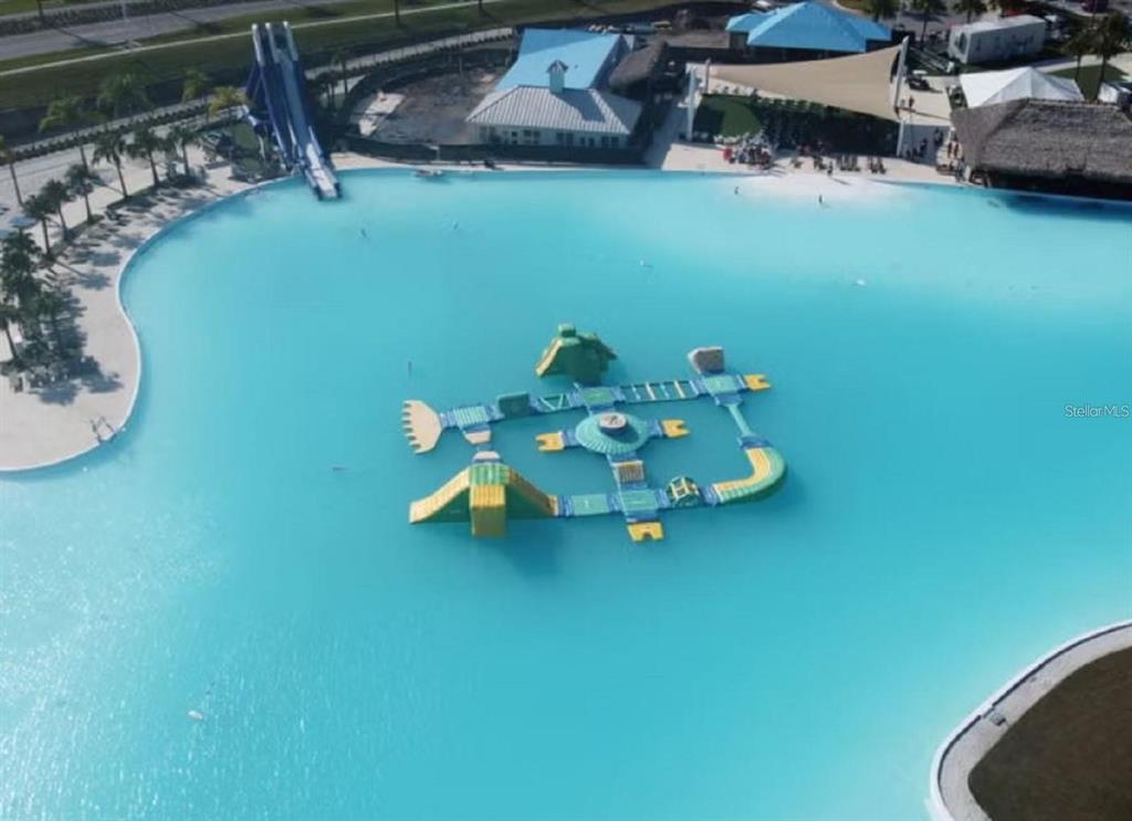 An aerial view of a large turquoise swimming lagoon with an inflatable obstacle course — 8132 SUNNY POINT TRAIL, PARRISH, FL