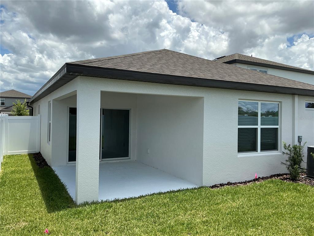 A white stucco house features a covered concrete patio and a sliding glass door — 3529 HORNBEAM ROAD, SPRING HILL, FL