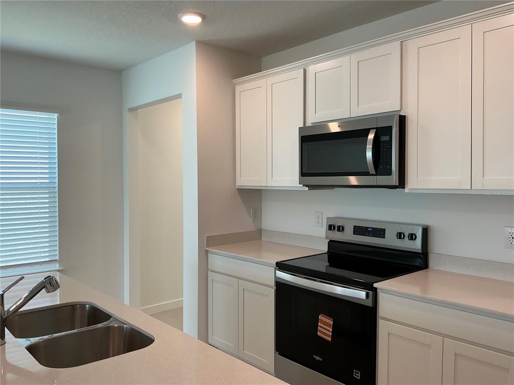 A kitchen features white cabinets, stainless steel appliances, and a double-basin sink in the island — 3529 HORNBEAM ROAD, SPRING HILL, FL