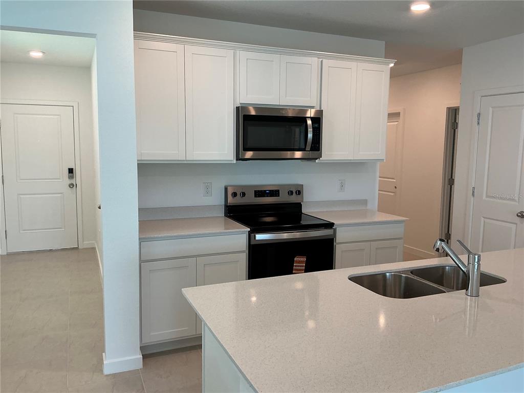 A kitchen features white cabinets, stainless steel appliances, and a light-colored quartz island countertop — 3529 HORNBEAM ROAD, SPRING HILL, FL