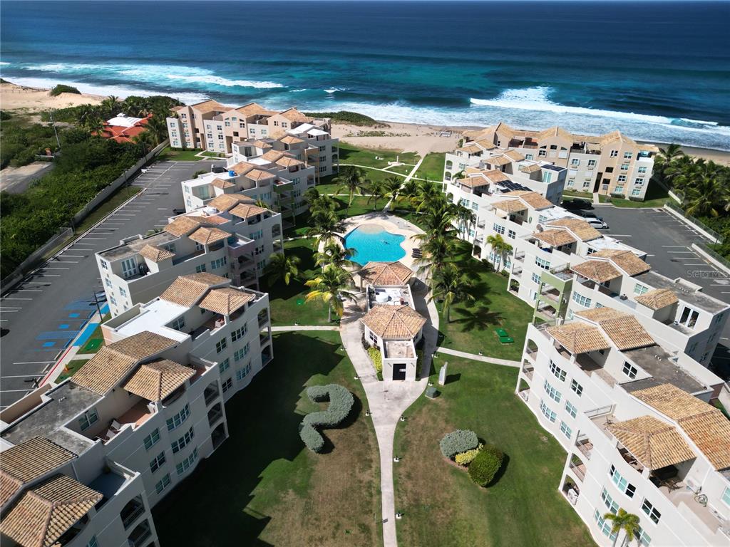 An aerial view of a beachfront apartment complex with a central pool and parking lots — Haudimar Beach Apartments PH UNIT G303, ISABELA, PR