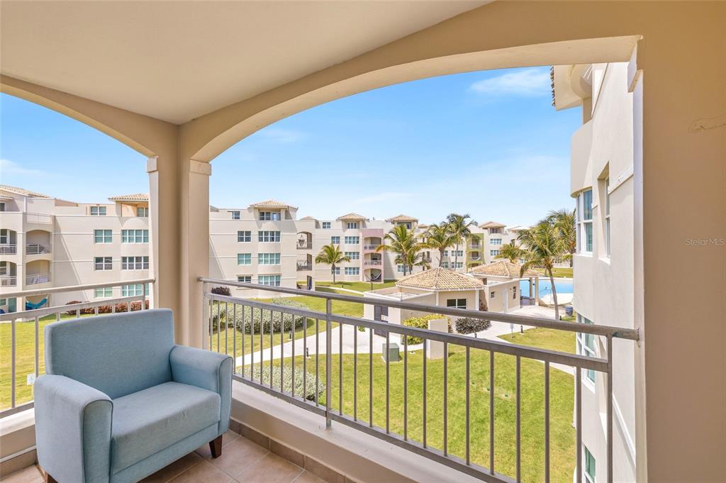 A balcony with a light blue armchair overlooks a courtyard with buildings and a pool — Haudimar Beach Apartments PH UNIT G303, ISABELA, PR