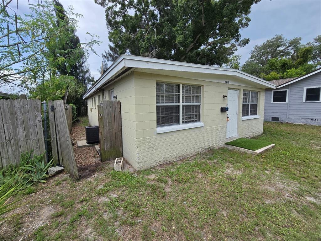 A small, light-colored concrete block house features a white front door and a wooden fence — 4426 13TH AVENUE S, ST PETERSBURG, FL