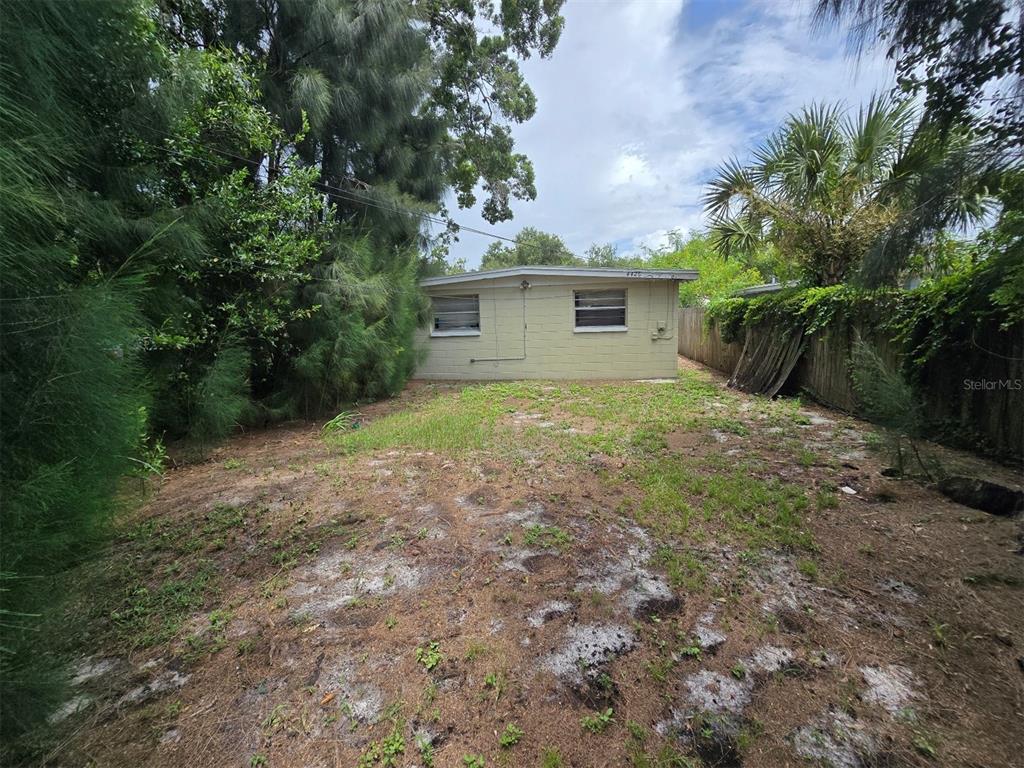 A view of a backyard featuring a single-story concrete block house and dense foliage — 4426 13TH AVENUE S, ST PETERSBURG, FL