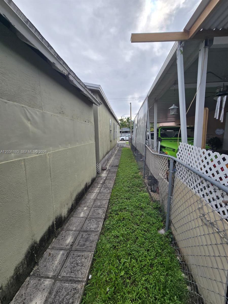 A narrow grassy walkway sits between a light-colored exterior wall and a chain-link fence — 1061 SW 131 PL, Miami FL 33184, MIAMI, FL