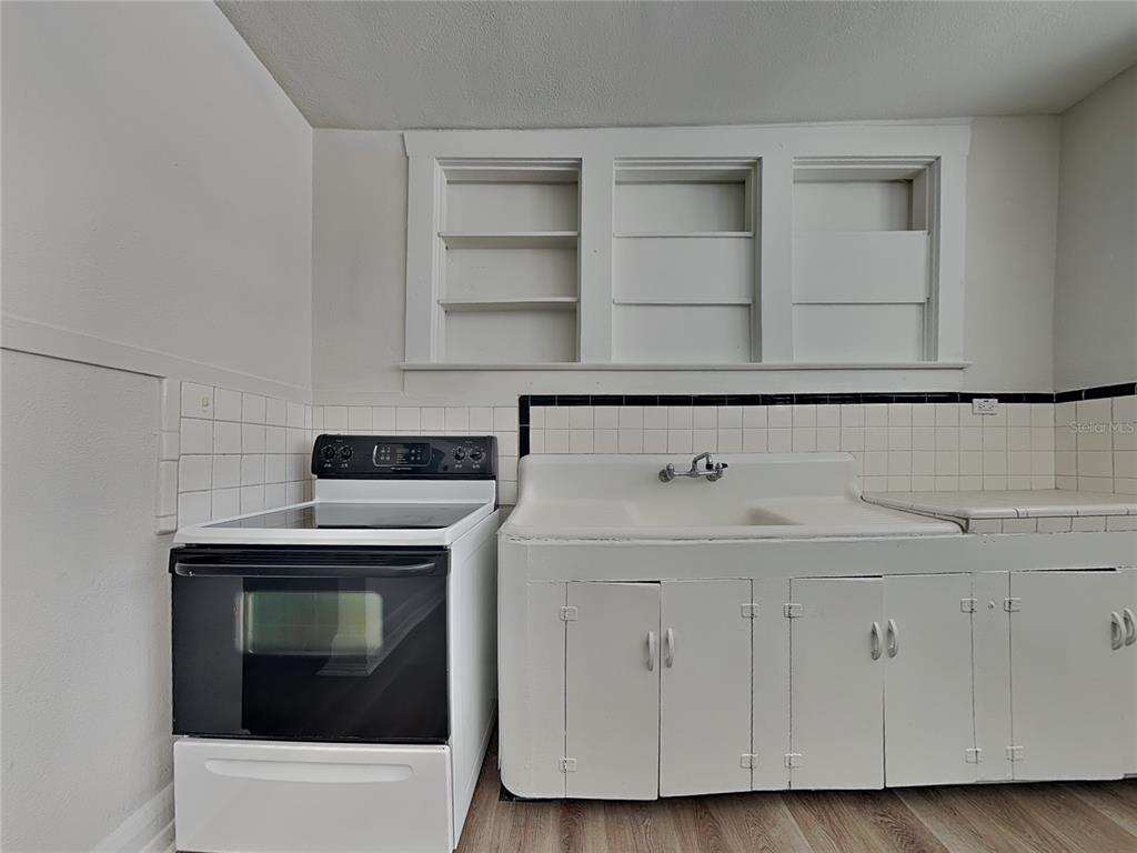 A kitchen features a white electric stove, a vintage farmhouse sink, and built-in wall shelving — 2904 W CHESTNUT STREET UNIT 2, TAMPA, FL