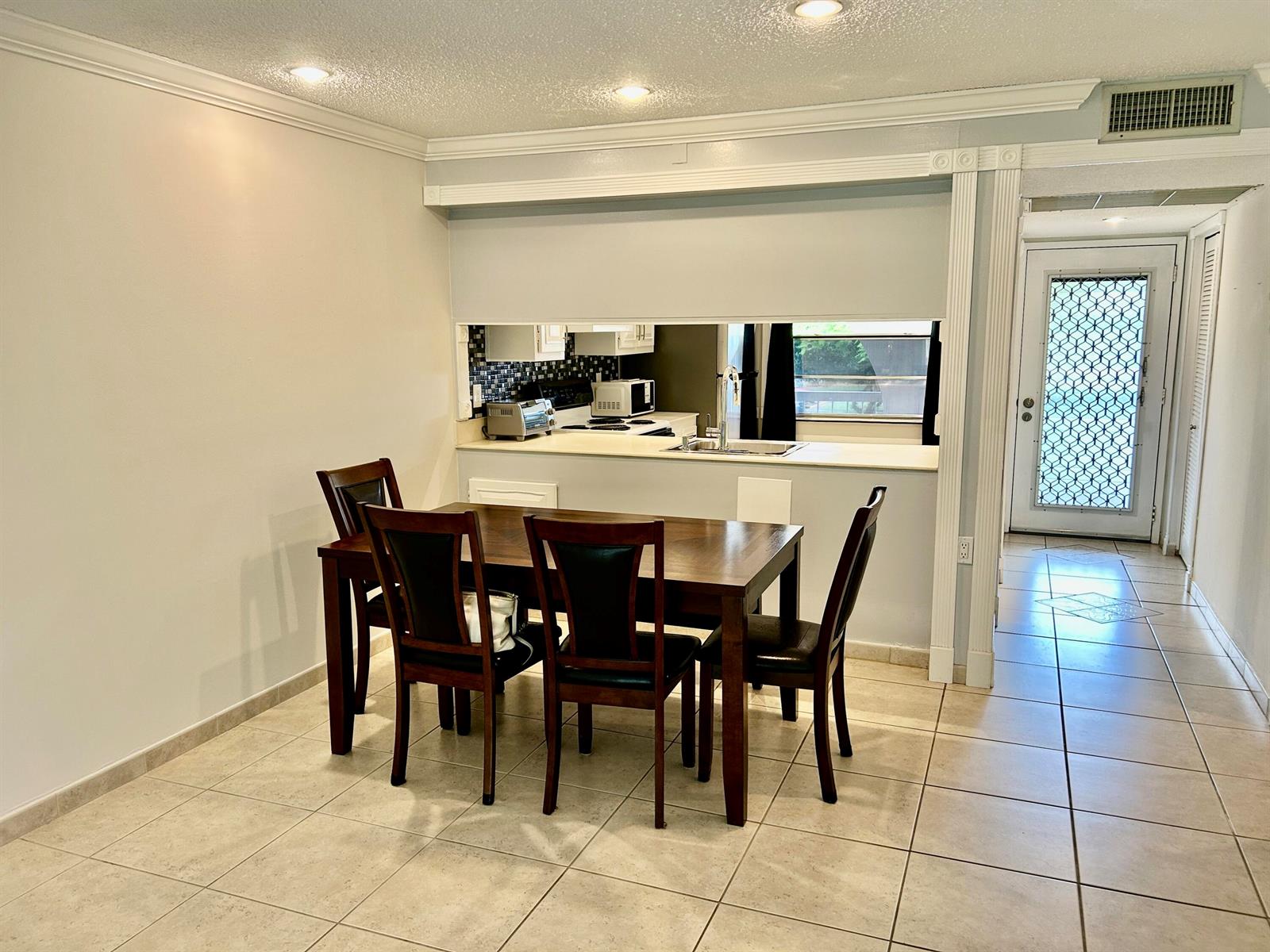 A dining area with a wooden table and chairs sits before a kitchen pass-through window — 2613 Nassau Bend # C2, Coconut Creek FL 33066, COCONUT CREEK, FL