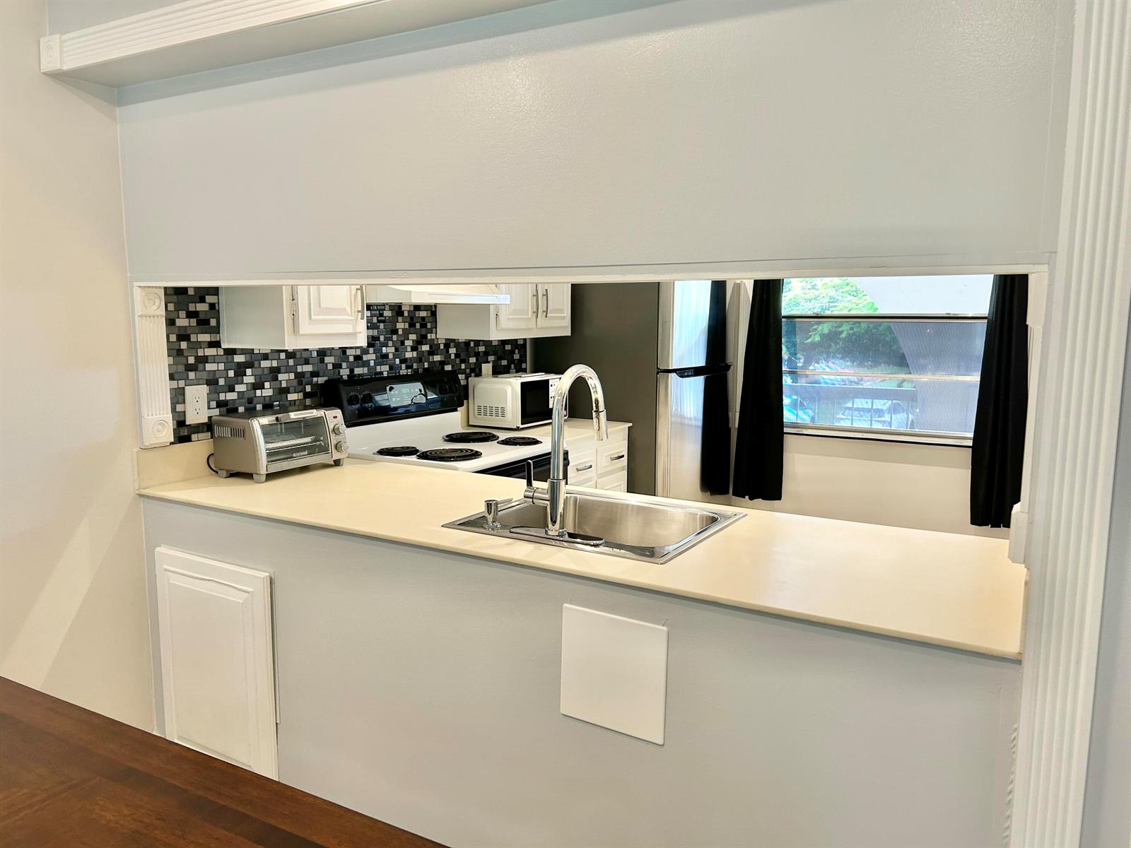 A kitchen features a pass-through window, stainless steel sink, and a mosaic tile backsplash — 2613 Nassau Bend # C2, Coconut Creek FL 33066, COCONUT CREEK, FL