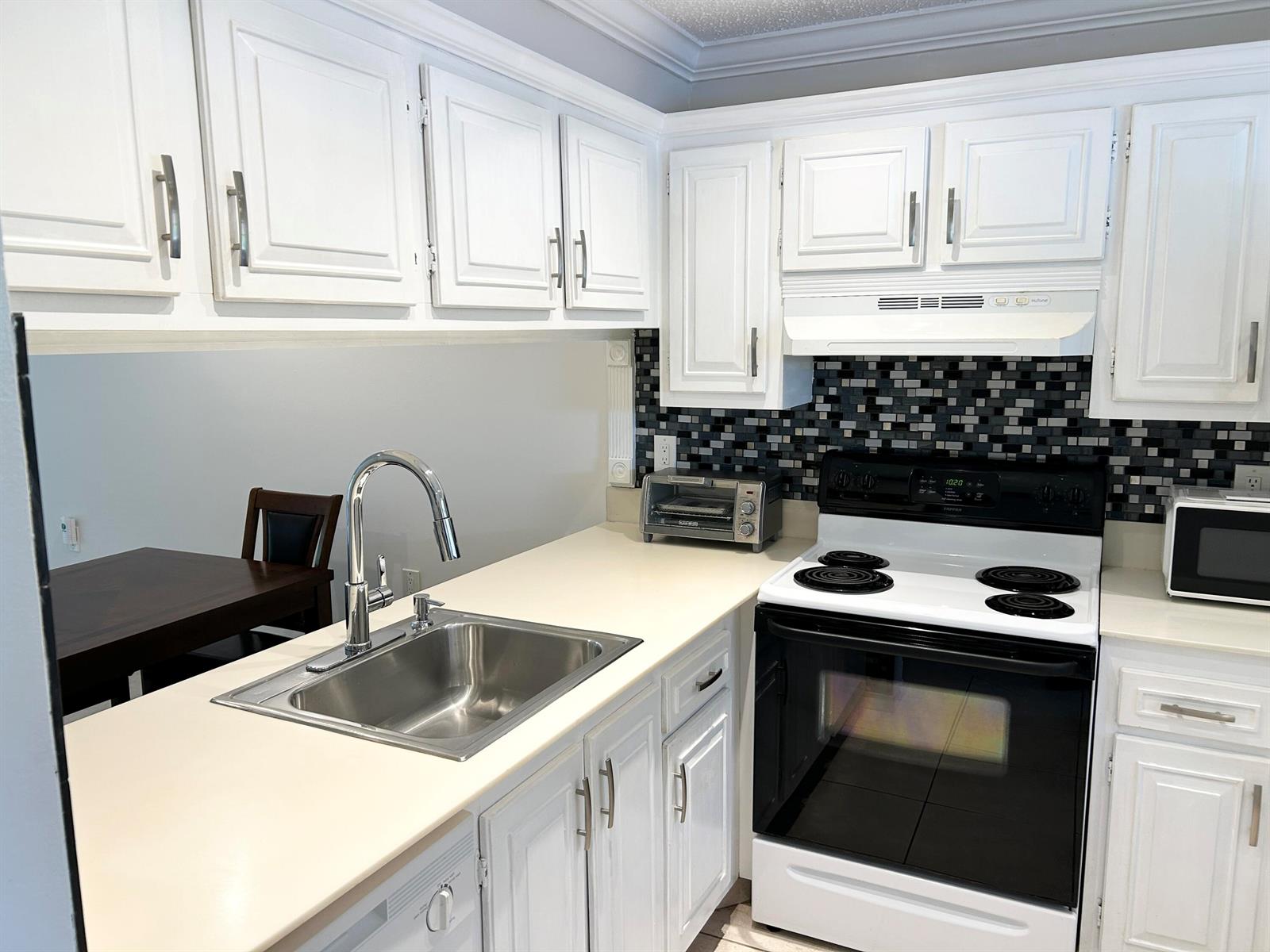 A kitchen features white cabinets, a stainless steel sink, a white stove, and tiled backsplash — 2613 Nassau Bend # C2, Coconut Creek FL 33066, COCONUT CREEK, FL