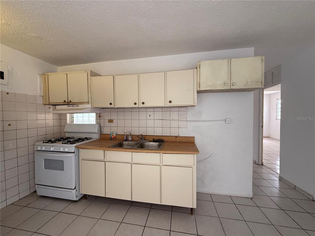 A kitchen features white cabinets, a gas stove, a double sink, and tiled walls and floors — 20 ST VILLA NUEVA UNIT W-41, CAGUAS, PR