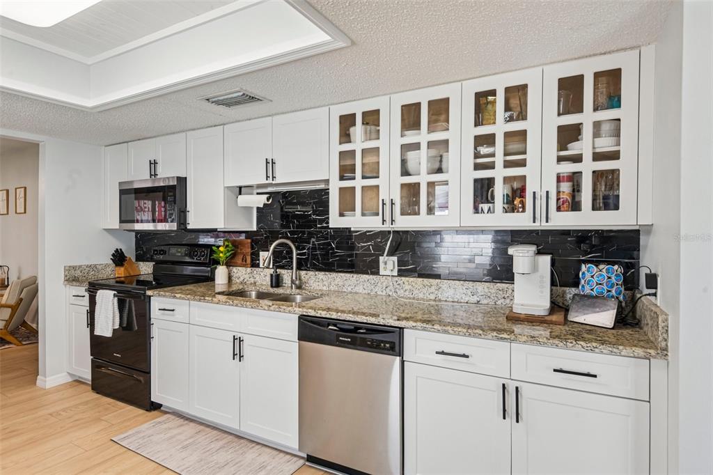 A kitchen with white cabinets, black marble-style backsplash, granite countertops, and stainless steel appliances — 11033 SALT TREE DRIVE, PORT RICHEY, FL