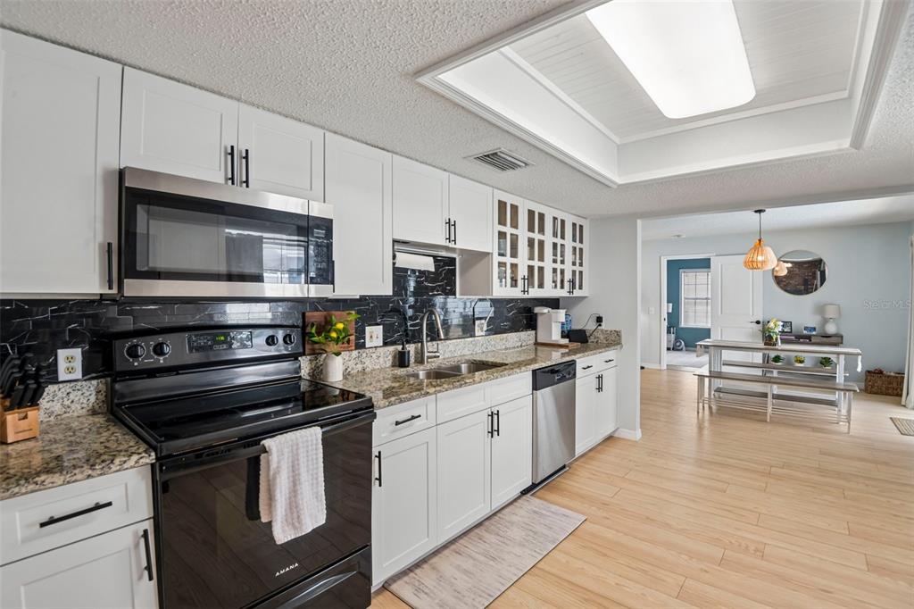 A kitchen with white cabinets, black tile backsplash, granite countertops, and stainless steel appliances — 11033 SALT TREE DRIVE, PORT RICHEY, FL