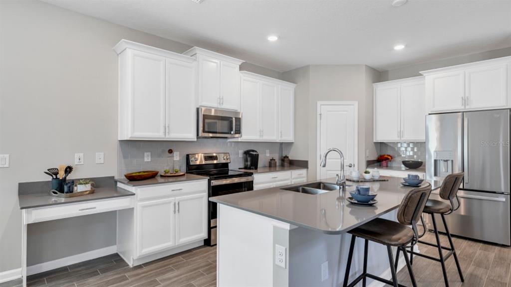 A modern kitchen features white cabinets, gray countertops, stainless steel appliances, and a central island — 5594 RONIN DRIVE, ST CLOUD, FL