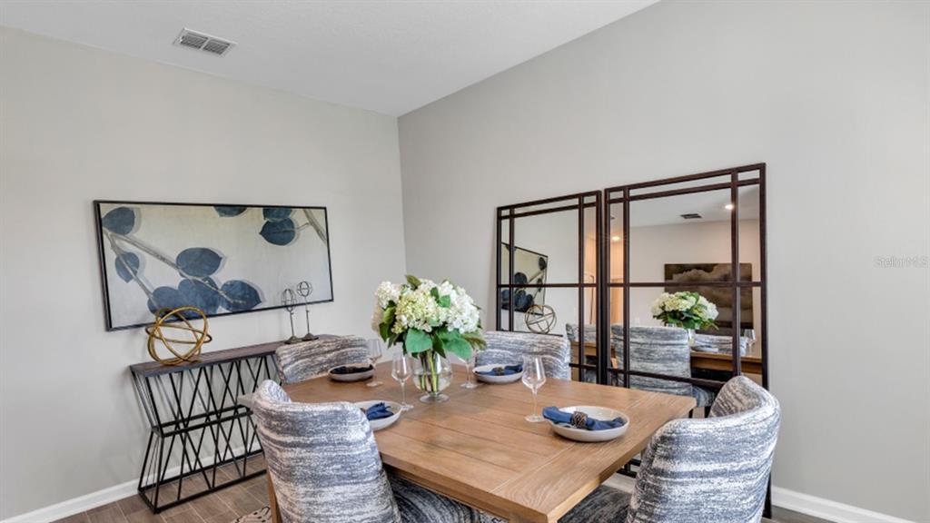 A dining room features a wooden table, upholstered chairs, a console table, and wall mirrors — 5594 RONIN DRIVE, ST CLOUD, FL