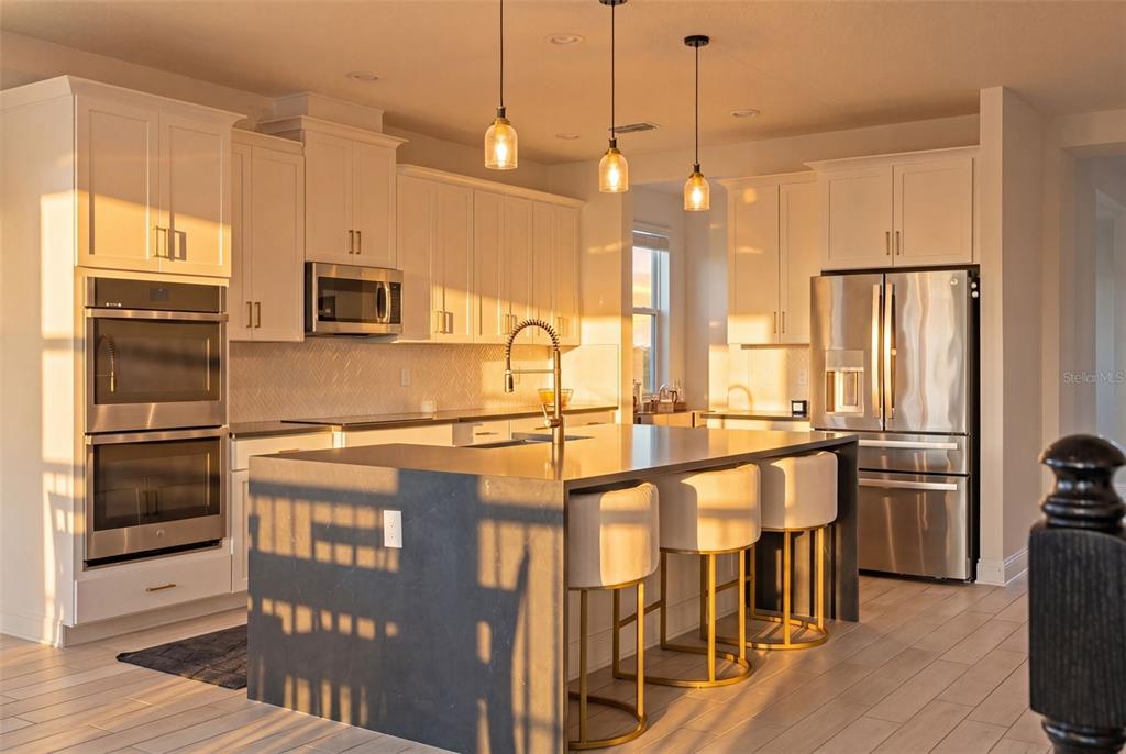 A modern kitchen features white cabinetry, a dark island with bar stools, and stainless appliances — 700 ALBYON COURT, DEBARY, FL