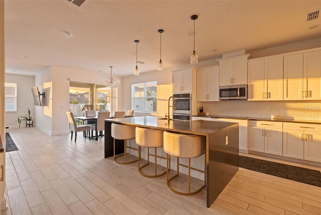 A modern kitchen features white cabinets, a dark island with bar stools, and tile flooring — 700 ALBYON COURT, DEBARY, FL