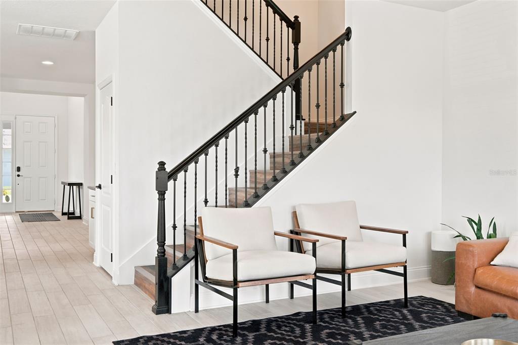 A staircase with black railings stands beside two armchairs on a patterned rug — 700 ALBYON COURT, DEBARY, FL