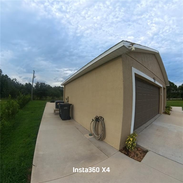 The exterior side of a tan garage features a concrete driveway, a hose, and trash cans — 25283 CANTERBURY DRIVE, LAKE WALES, FL