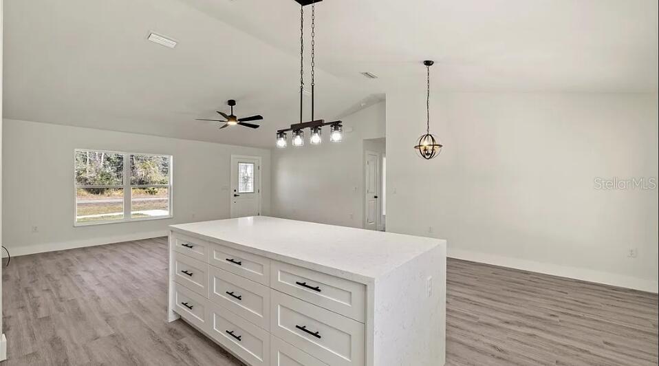 A kitchen island with white cabinets and a quartz countertop sits in an open-concept room — 130 HALLMARK AVENUE, LAKE PLACID, FL