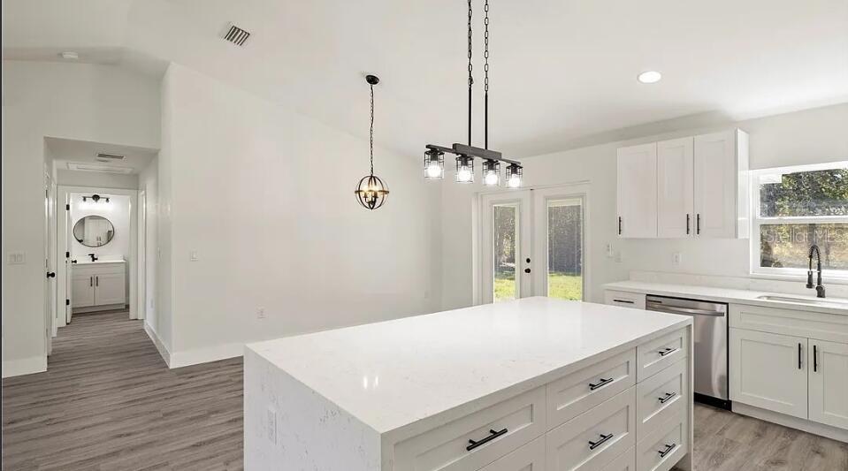 A modern kitchen features a large white quartz island, white cabinetry, and light wood flooring — 130 HALLMARK AVENUE, LAKE PLACID, FL