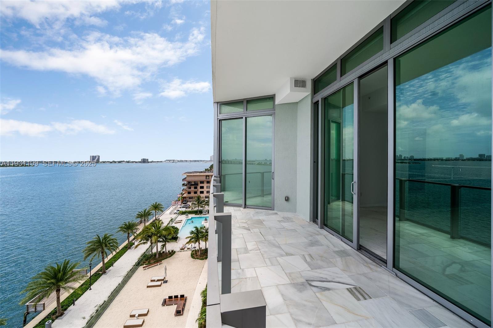 A balcony with marble flooring overlooks a swimming pool, sandy area, and the ocean — 2900 NE 7th Ave # 604, Miami FL 33137, MIAMI, FL