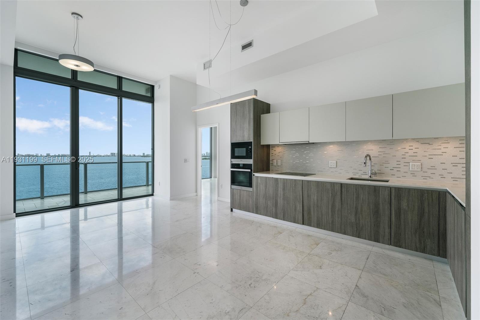 A modern kitchen with wood-grain cabinetry and marble floors overlooks the ocean through floor-to-ceiling windows — 2900 NE 7th Ave # 604, Miami FL 33137, MIAMI, FL