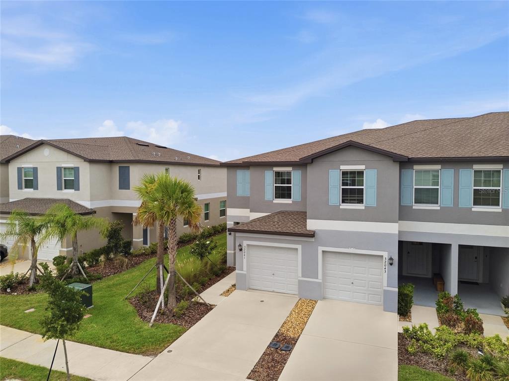 An exterior view of two adjacent two-story townhomes with gray siding and attached garages — 32041 POWDERPUFF MIMOSA DRIVE, SAN ANTONIO, FL