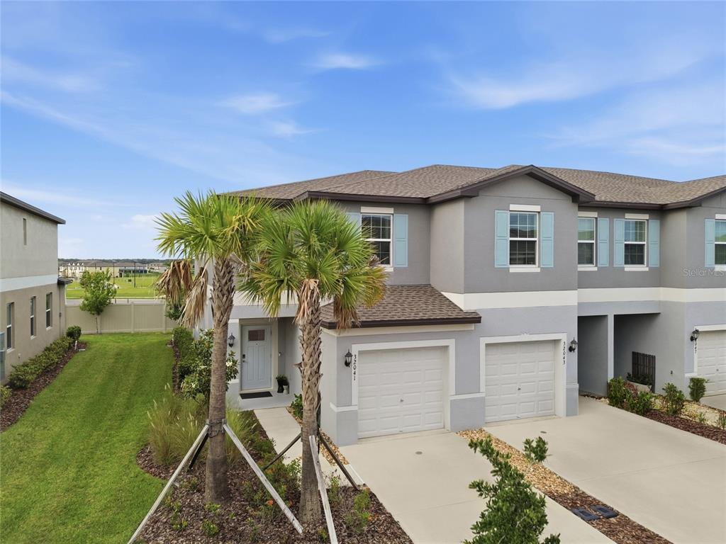 An exterior view of a two-story gray townhouse with two garage doors and palm trees — 32041 POWDERPUFF MIMOSA DRIVE, SAN ANTONIO, FL