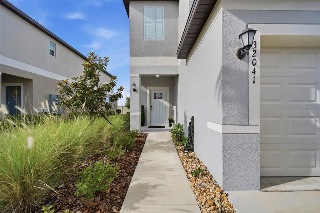A concrete walkway leads to the front entrance of a two-story house with a garage — 32041 POWDERPUFF MIMOSA DRIVE, SAN ANTONIO, FL